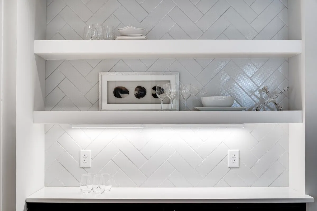 A stylish set of white shelves adorned with curated glassware, framed artwork, and decorative elements. The space exudes sophistication and is designed for entertaining guests, highlighting the personal touches that make the area feel special.