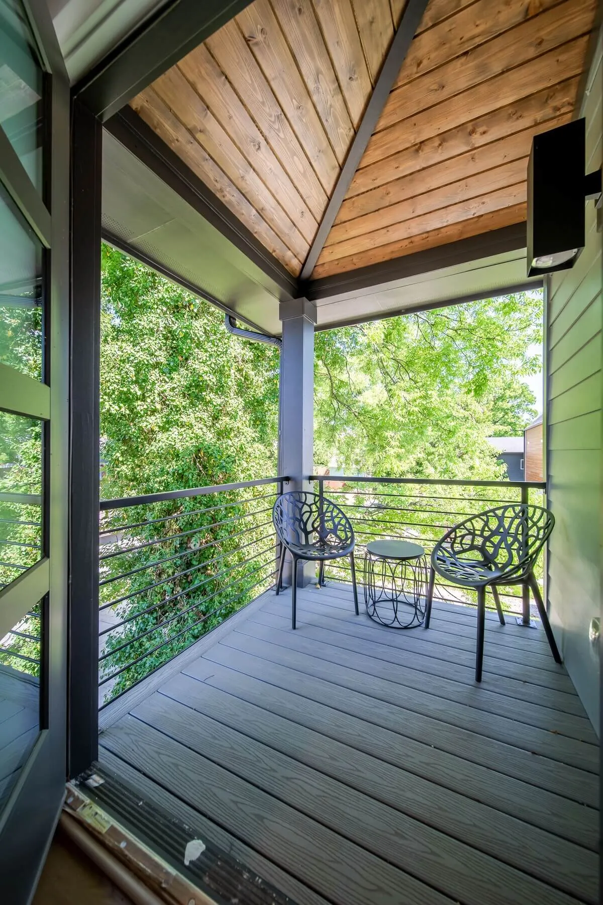 A tranquil balcony scene featuring comfortable chairs and a table surrounded by lush greenery. The setup invites guests to relax with a morning coffee or evening drink while overlooking the neighborhood.