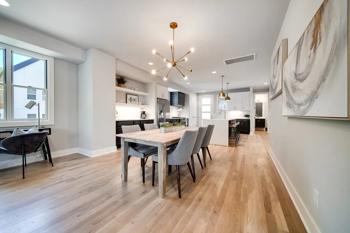 An inviting dining area anchored by a modern table and chandelier, situated adjacent to a kitchen island. The layout is designed for both family meals and entertaining guests, with cozy lighting and tasteful decor enhancing the welcoming mood.