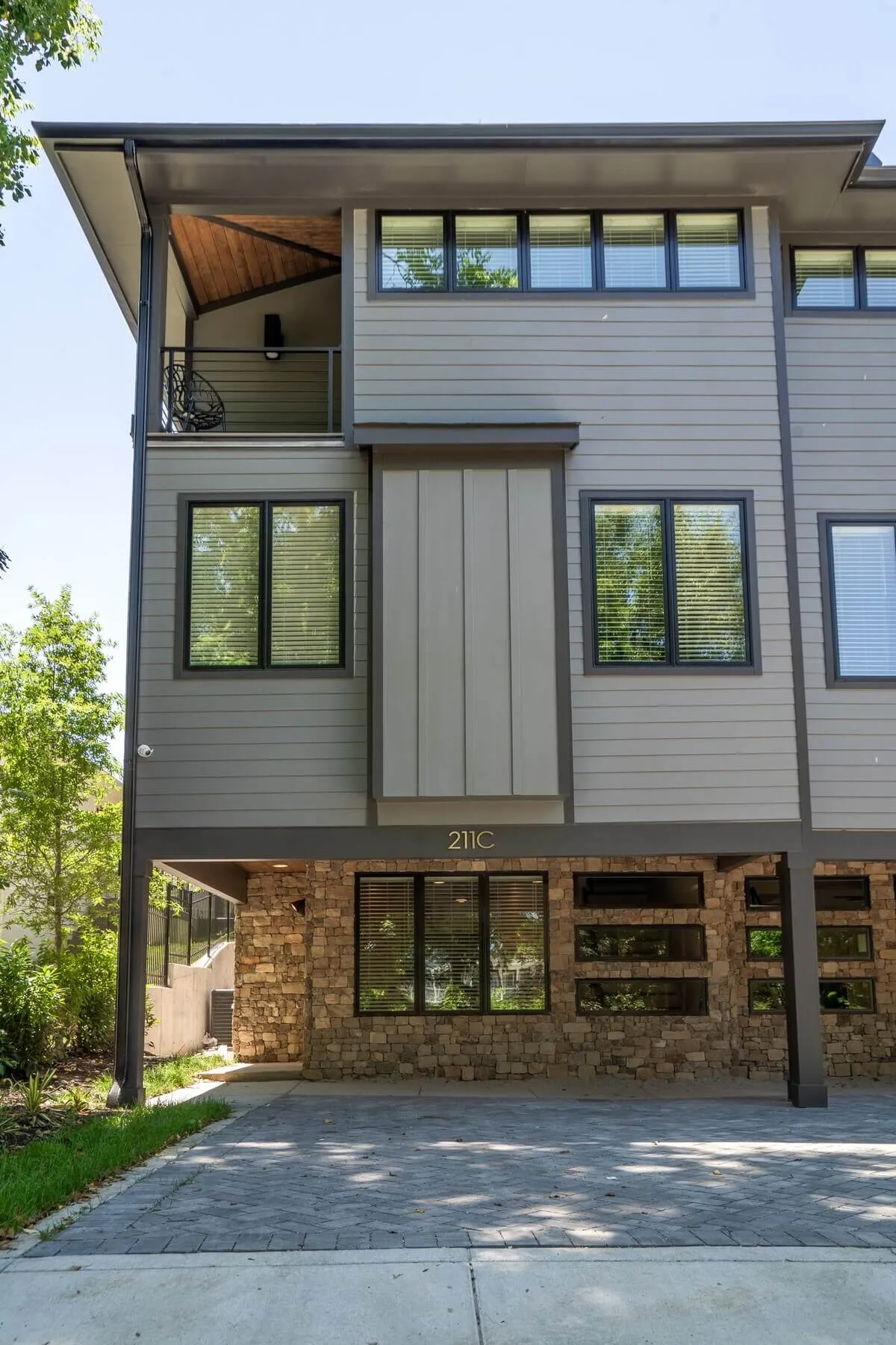 A contemporary exterior shot of the home, showcasing its stone base, modern upper structure, and a balcony with a view. Landscaped areas and the inviting outdoor space draw the eye, suggesting a vibrant connection to the neighborhood and city beyond.