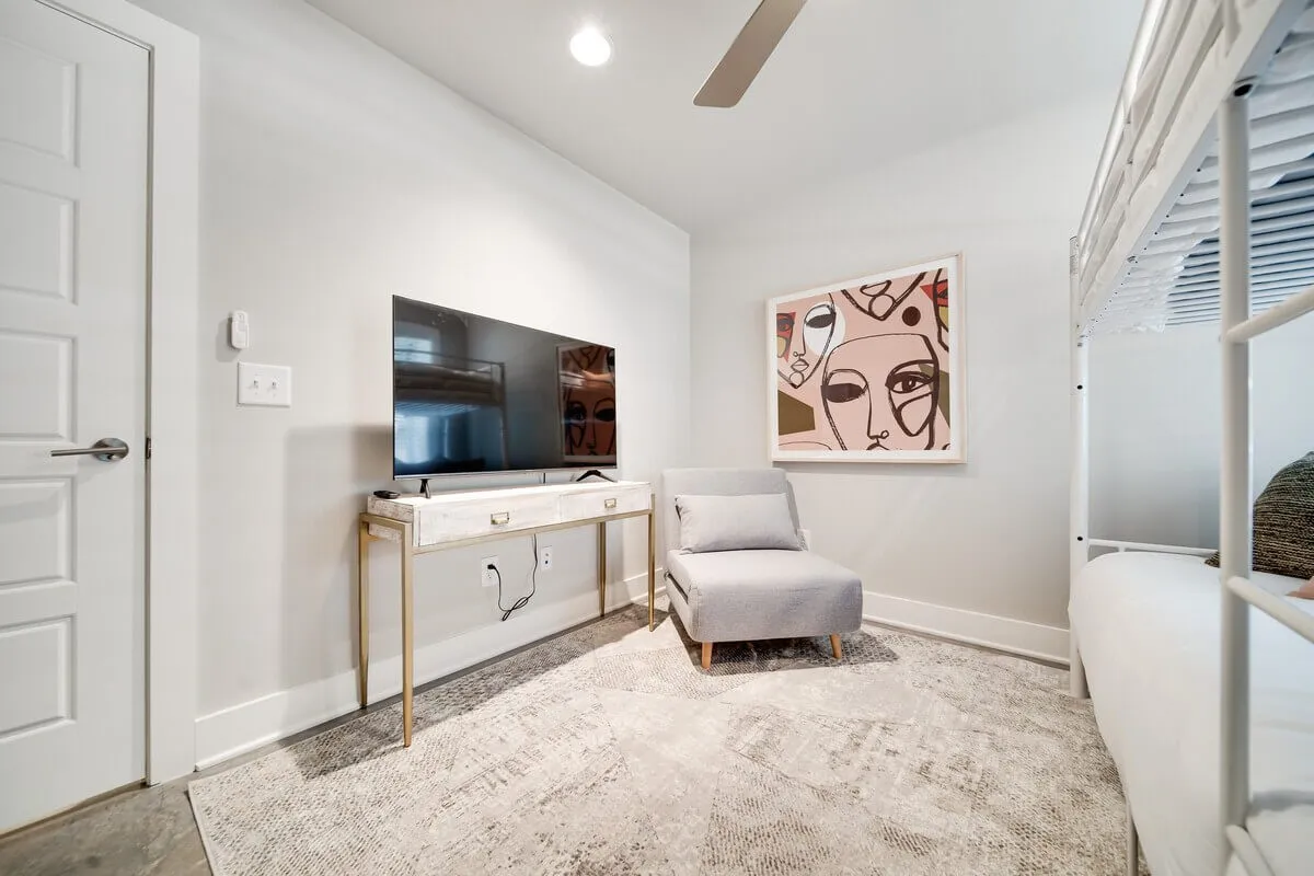 A contemporary, cozy room with a television, armchair, modern artwork, and a bunk bed. The space is warm and welcoming, suitable for guests to relax, catch up on highlights, or enjoy an intimate movie night together.