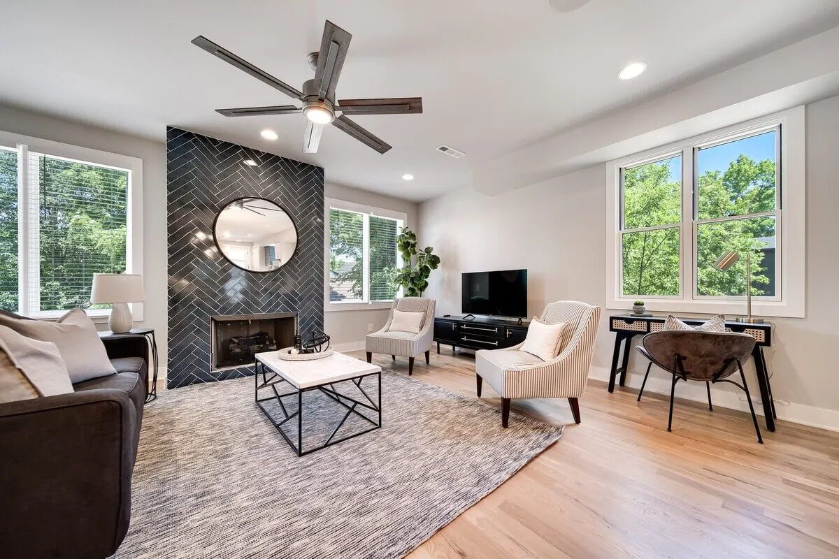 A contemporary living area featuring a patterned feature wall, a round mirror, a central coffee table, and an inviting seating arrangement. The room is styled with plush cushions, designer accents, and offers a bright, open feel ideal for socializing or relaxing.