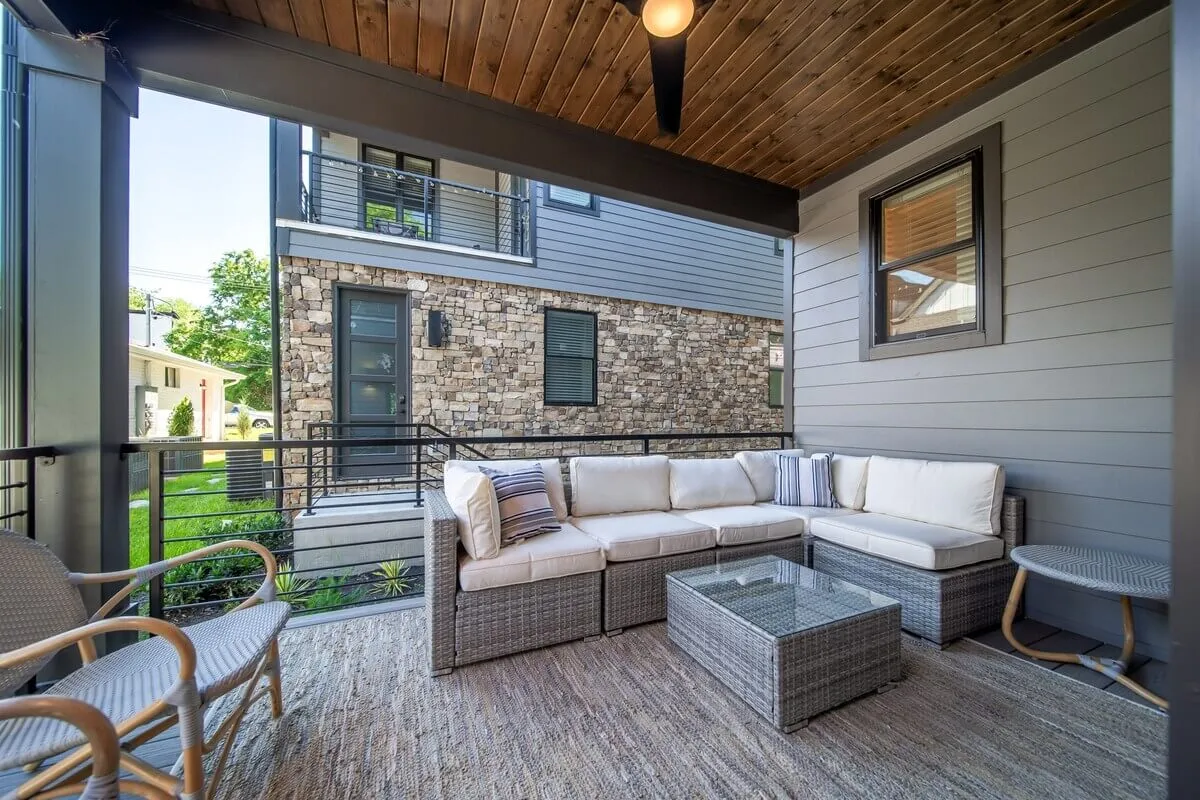 A stylish outdoor patio featuring a comfortable sectional sofa, a glass coffee table, and a woven rug, all set against an inviting outdoor view. Warm lighting and lush touches contribute to a cozy, welcoming atmosphere suitable for relaxation or entertaining guests. The patio is private and feels like a true retreat within the city.