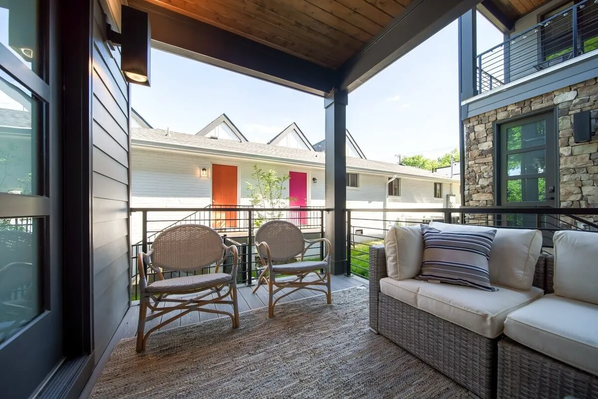 An inviting exterior communal patio space with two wicker chairs and a cushioned sofa, set against colorful doors. The environment suggests a spot for socializing or enjoying the fresh air before heading out or after returning from the city.