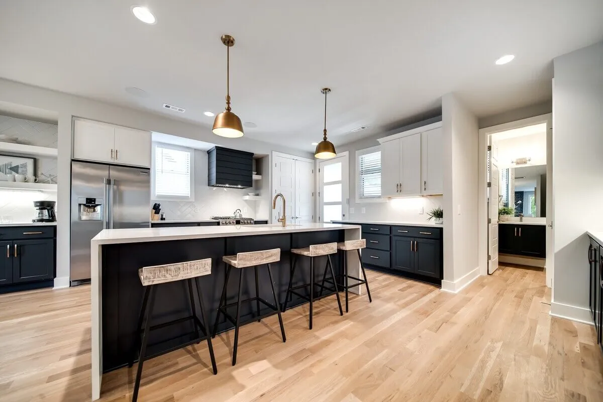 A contemporary kitchen with a large central island, gold pendant lights, and a striking mix of dark and light cabinetry. The layout provides ample prep space, modern appliances, and plenty of room for hosting and cooking together.